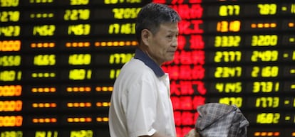 Un inversor pasa delante de una pantalla que muestra la cotizaci&oacute;n de varios valores en una oficina de corretaje en Huaibei (China)