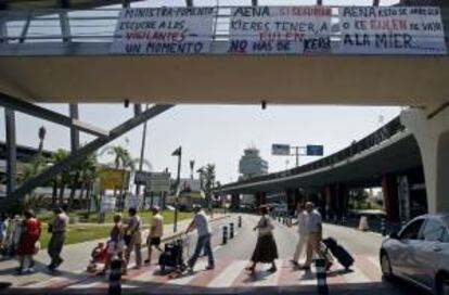 Un grupo de pasajeros pasa ante varias pancartas reivindicativas desplegadas por los vigilantes de seguridad de la empresa Eulen del aeropuerto de Manises (Valencia). EFE/Archivo