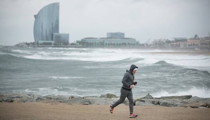 Un home corre per un espigó de la Barceloneta durant el temporal.