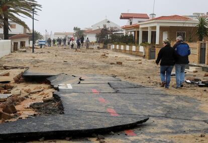 Vecinos de La Antilla (Huelva), una de las zonas más castigadas por el temporal, caminando por una calle destrozada de este núcleo urbano. Se ha prohibido la entrada a 30 viviendas por precaución. 