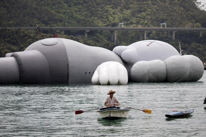 Un pescador pasa con su bote cerca de la escultura hinchable de 37 metros de largo 'KAWS:HOLIDAY', obra del artista estadounidense Brian Donnelly, también conocido como 'Kaws', en Tsing Yi, Hong Kong. La pieza se exhibirá en el Puerto Victoria del Hong Kong del 22 al 31 de marzo. 