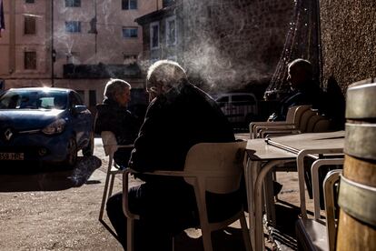 Tres hombres toman café al sol en un bar de Villel, Teruel.