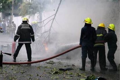 Varios bomberos apagan el coche bomba en llamas tras la explosión que ha matado a 7 personas en la capital.