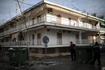 Dos bomberos trasladan un contenedor de basura junto a los escombros después de fuertes tormentas.

