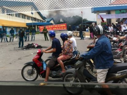 Motoristas pasan ante los polic&iacute;as que vigilan la zona donde se encuentra una factor&iacute;a incendiada en la provincia vietnamita de Binh Duong.