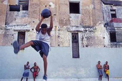 Unos jóvenes habaneros juegan al baloncesto con el trasfondo de un desvencijado edificio.