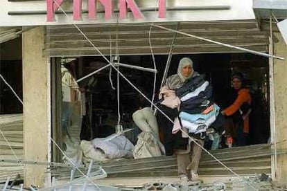 Dos mujeres libanesas sacan la mercancía de una tienda de ropa destruida por las bombas de la aviación israelí.