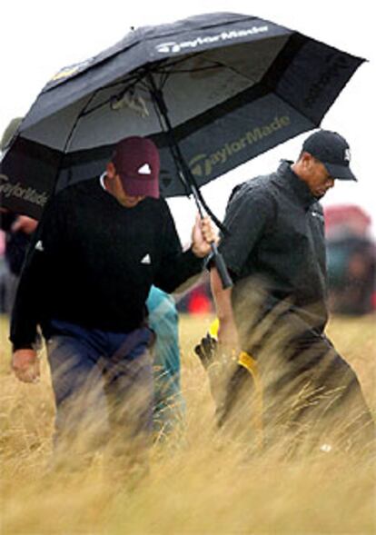 Tiger Woods, a la derecha, protegido de la lluvia.