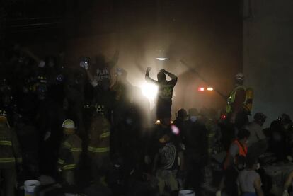 Bomberos mexicanos alzan los brazos para indicar a la multitud la posible presencia de supervivientes.