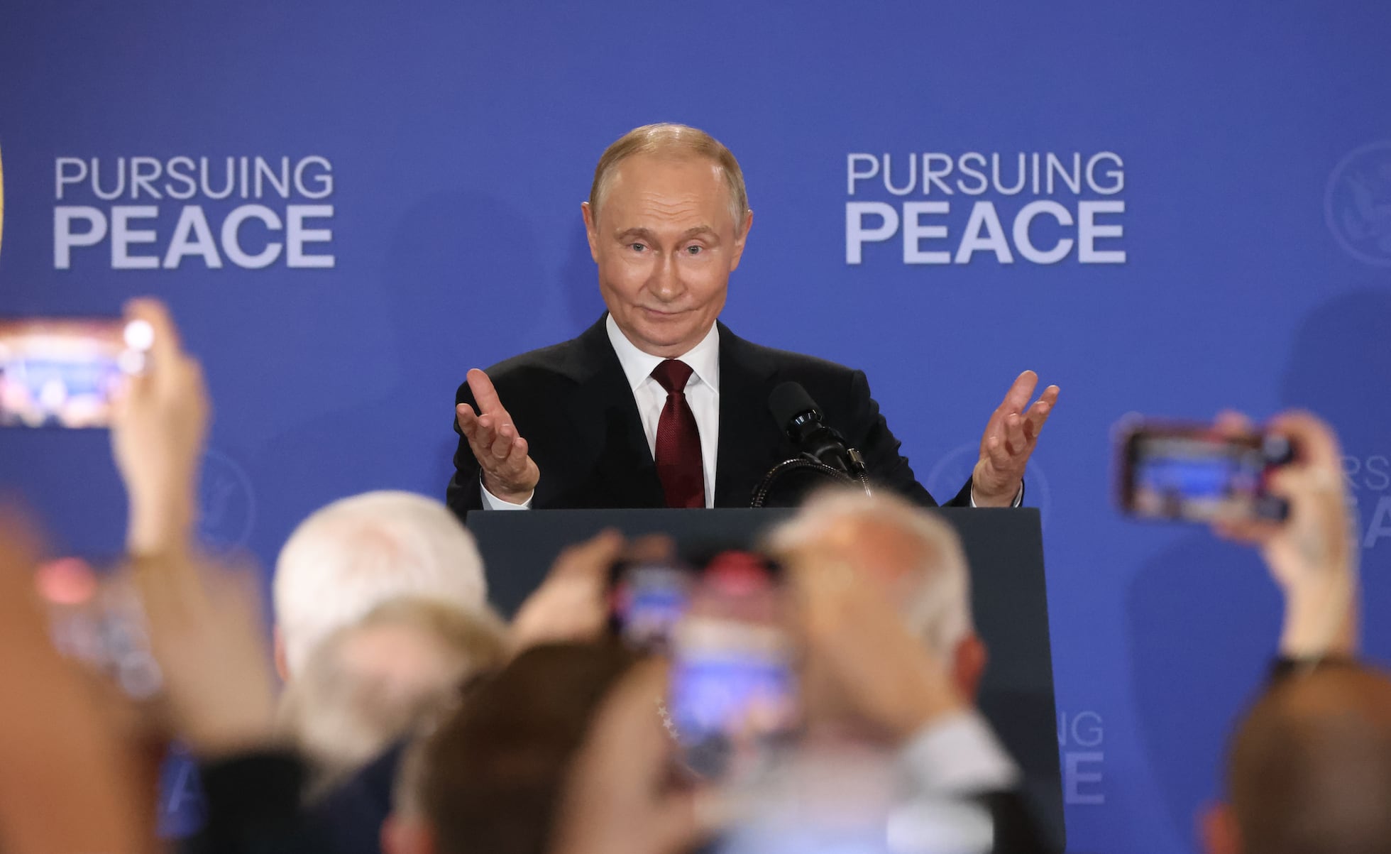 Putin at Alaska meeting speaking under “Pursuing Peace” banner, symbolizing hypocrisy and U.S. betrayal