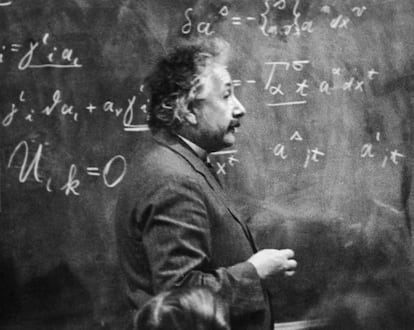 El físico Albert Einstein (1879 - 1955) de pie junto a una pizarra con cálculos matemáticos escritos con tiza.