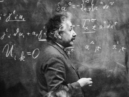El físico Albert Einstein (1879 - 1955) de pie junto a una pizarra con cálculos matemáticos escritos con tiza.