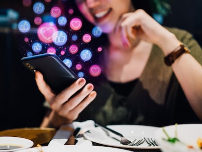 Joven sonriente usando un smartphone en una aplicación de redes sociales mientras disfruta de una comida en el restaurante, mirando o dando 'me gusta', amor, comentarios, agregando amigos y visitando páginas. Concepto de adicción a las redes sociales.