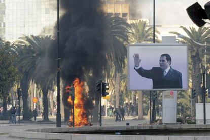 Un incendio causado por unos manifestantes cerca de un cartel de Ben Ali en una calle de Túnez.
