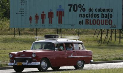 Un antiguo coche de fabricaci&oacute;n estadounidense pasa ante un cartel sobre el bloqueo a la isla en La Habana.