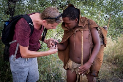 Un turista pone a Wame su reloj de pulsera. Aunque en la imagen el choque cultural parezca muy evidente, en realidad no es así, pues chicos como Wame visten a la manera occidental cuando no están trabajando. Su generación ya ha sido educada en escuelas corrientes, saben inglés y están al día de las comodidades y artilugios de la vida moderna. Esta entrada en el sistema preocupa a los defensores de la cultura bosquimana: Por ejemplo, el hecho de estudiar en un colegio donde no se imparten clases de khoisan, la lengua nativa de esta comunidad, hará que al final acabe desapareciendo.