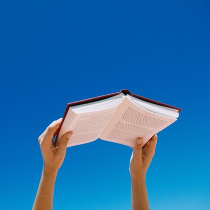 Young woman holding book up in air, low angle view