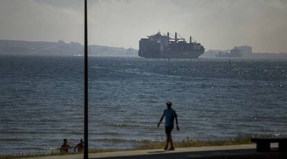 Un hombre pasea por una playa de Algeciras mientras dos ba&ntilde;istas salen del agua.