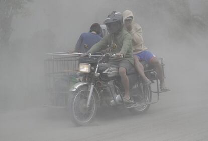Una conduce su motocicleta a través de nubes de cenizas mientras evacúan a terrenos más seguros, el lunes 13 de enero.