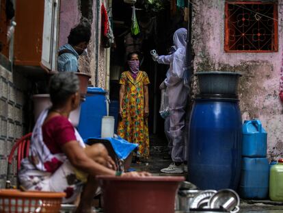 Un sanitario indio con un traje de protección comprueba la temperatura, oxígeno en sangre y pulsaciones de una residente en una de las zonas más afectadas por la covid-19 en Bombay el 1 de julio.