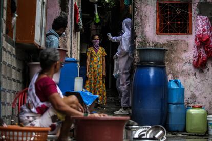 Un sanitario indio con un traje de protección comprueba la temperatura, oxígeno en sangre y pulsaciones de una residente en una de las zonas más afectadas por la covid-19 en Bombay el 1 de julio.