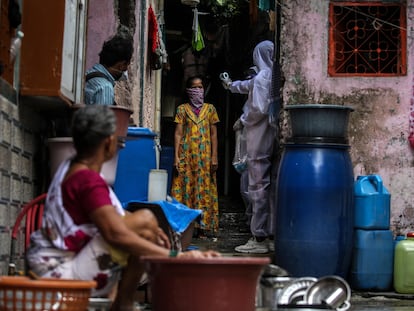 Un sanitario indio con un traje de protección comprueba la temperatura, oxígeno en sangre y pulsaciones de una residente en una de las zonas más afectadas por la covid-19 en Bombay el 1 de julio.