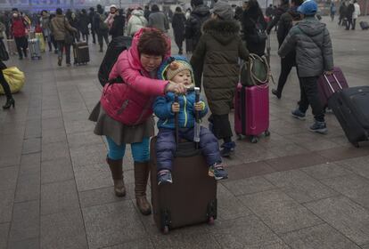 Una mujer lleva a su hijo sobre una maleta de camino a la estación de tren de Pekín.