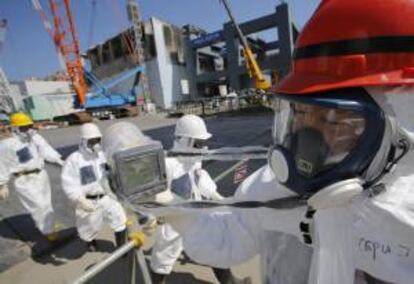 Un trabajador de la operadora Tokyo Electric Power (TEPCO) sostiene un monitor de radiación junto al reactor número 4 (atrás izq) durante una visita a la planta nuclear de TEPCO en Fukushima, Japón. EFE/Archivo
