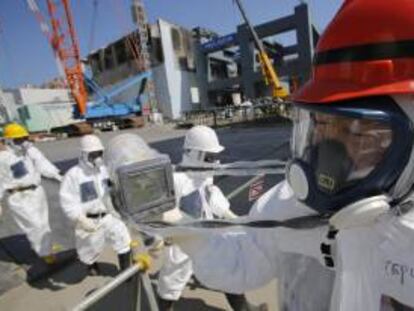 Un trabajador de la operadora Tokyo Electric Power (TEPCO) sostiene un monitor de radiación junto al reactor número 4 (atrás izq) durante una visita a la planta nuclear de TEPCO en Fukushima, Japón. EFE/Archivo