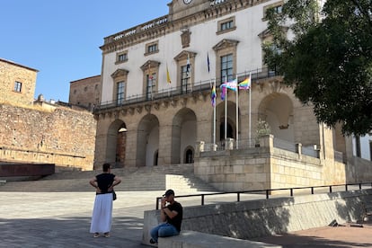 Varias personas junto al Ayuntamiento de Cáceres donde ondean las banderas del Orgullo LGTBI, este domingo antes de la procesión del Corpus Christi.