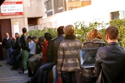 Un joven consulta su ordenador mientras guarda cola ante una oficinia de empleo.