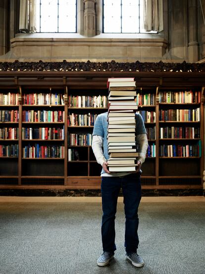 Extra Formación 08 Mayo Young man carrying stack of books in university library