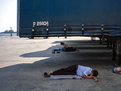 Unos hombres descansan bajo unos camiones en el puerto del Pireo, donde casi 1.500 refugiados y migrantes viven en un campamento improvisado.