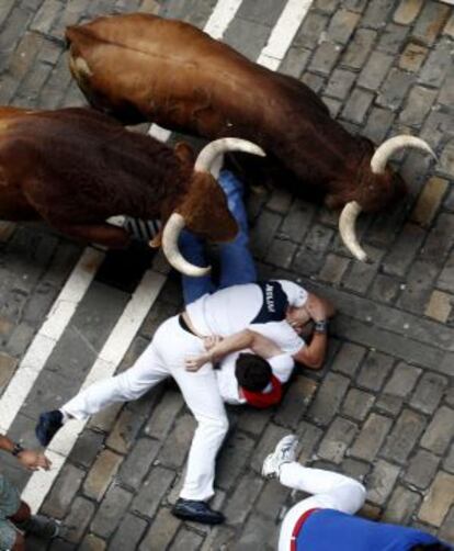 Dos toros de la ganadería salmantina de El Pilar pasan por encima de dos mozos caídos durante su carrera por el tramo de la Calle Estafeta.