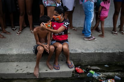 Uma menina ajuda um menino a colocar uma máscara doada enquanto os moradores fazem fila para receber sacolas de comida grátis, no Rio de Janeiro.