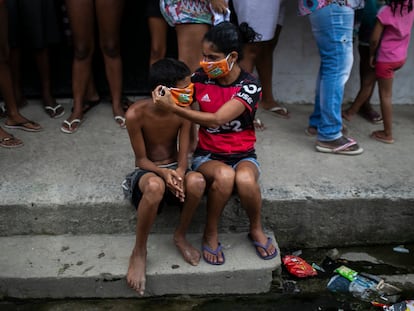 Uma menina ajuda um menino a colocar uma máscara doada enquanto os moradores fazem fila para receber sacolas de comida grátis, no Rio de Janeiro.