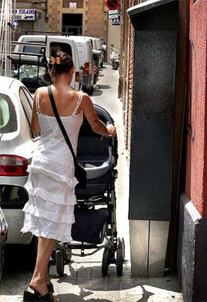 Apuros de una mujer para pasar con un cochecito en un tramo de acera con parquímetro.