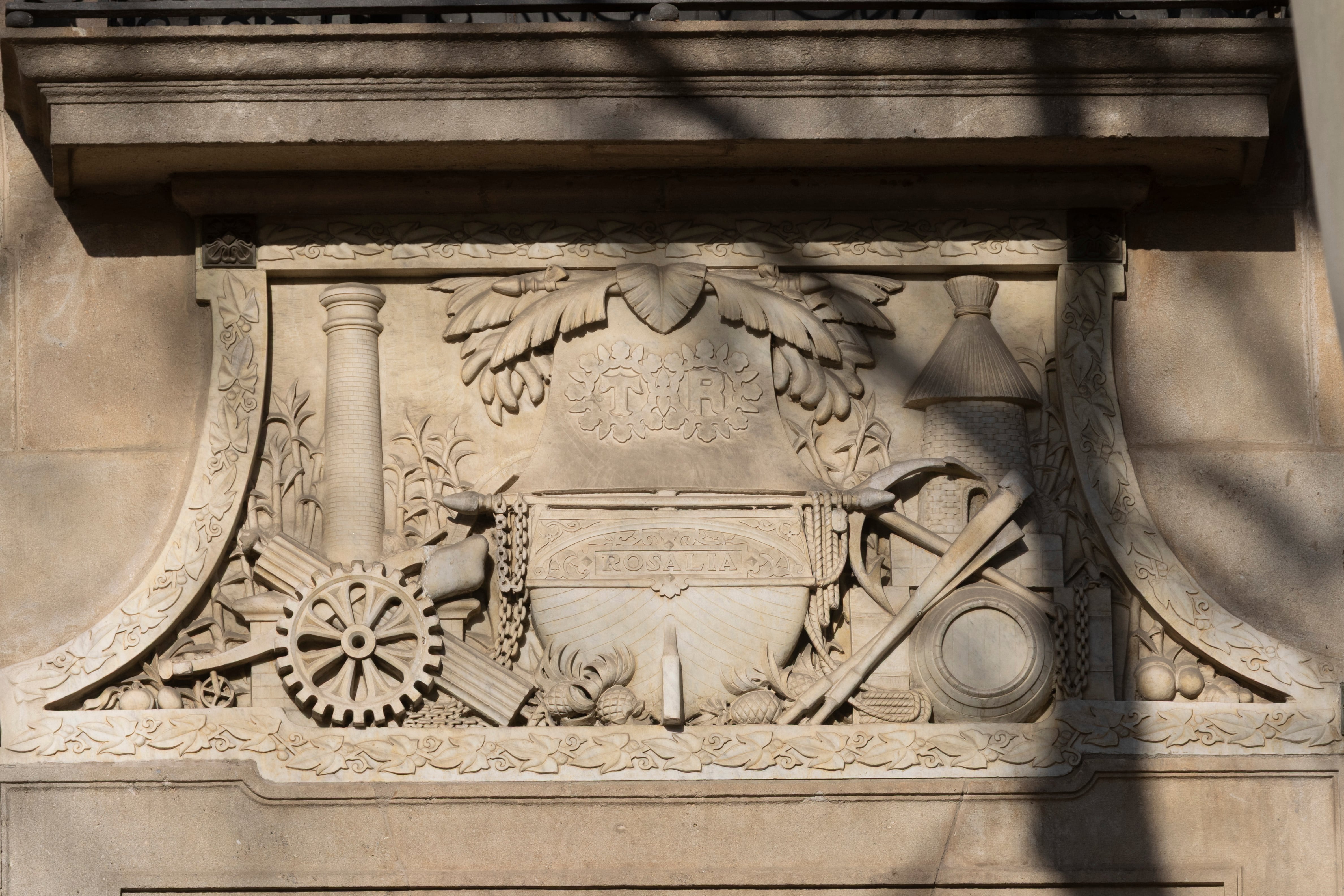 Bajorrelieve en la fachada del Palau Marc de Barcelona, en el que se aprecian las iniciales  T. R. (Tomas Ribalta) y cadenas, sogas, cañas de azúcar y una chimenea. 
CARLES RIBAS