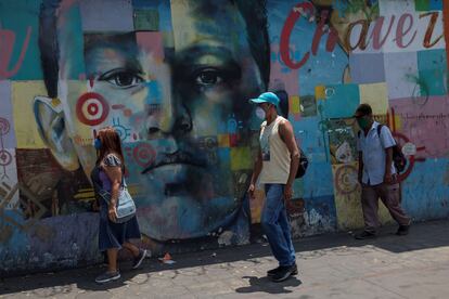 Tres personas con tapabocas caminan frente a un mural de Hugo Chávez, el 3 de marzo en Caracas, Venezuela.