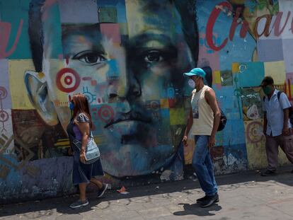 Tres personas con tapabocas caminan frente a un mural de Hugo Chávez, el 3 de marzo en Caracas, Venezuela.