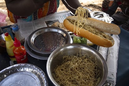 Bintou prepara un bocadillo de espagueti con salsa de cebolla y picante para un cliente matutino. “Desde que abro el puesto a las siete y hasta que lo cierro, no paro de trabajar. Hay varias obras cerca de aquí y todos los obreros vienen a buscar su desayuno. Bocadillos de pasta, de guisantes, de huevo o tortilla francesa con salsas de cebolla, patata, atún y picante, mucho picante. Después de los obreros, empiezan los turnos de recreo de los colegios, ¡es un no parar!”, comenta.