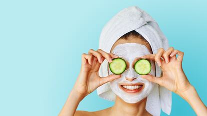 Beautiful young woman with facial mask on her face holding slices of cucumber