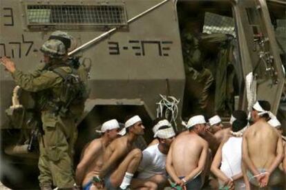 Varios presos palestinos en ropa interior esperan maniatados junto a un blindado del Ejército de Israel.