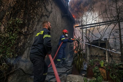 Bomberos intentan extinguir el fuego en una vivienda afectado por el incendio forestal de Dionysos, este lunes. 