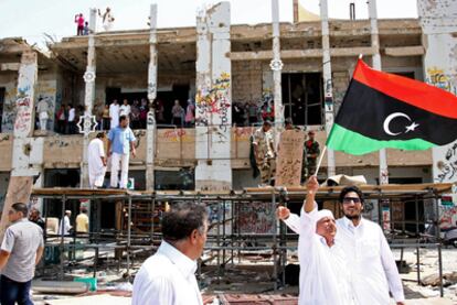Un hombre ondea la bandera de la rebelión mientras numerosos tripolitanos visitan el fortín de Gadafi en Bab el Azizia.