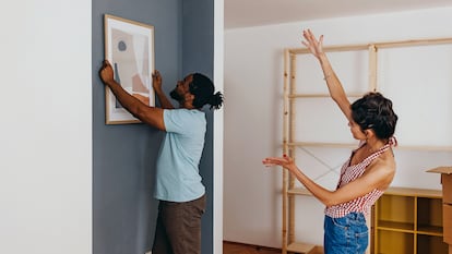 Una pareja colgando un cuadro en su casa.