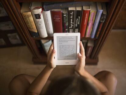Una noia llegeix un 'e-book' junt amb diversos llibres.