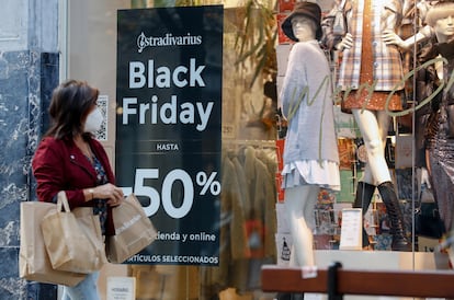Una mujer pasea frente a una tienda que anuncia descuentos el día del Black Friday.