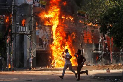 Dos hombres corren frente a un centro comercial incendiado durante las protestas de este domingo contra la primera ministra Sheikh Hasima.
