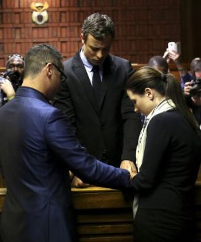 Oscar Pistorius, durante la vista, de la mano con sus hermanos Aimee y Carl, rezando.